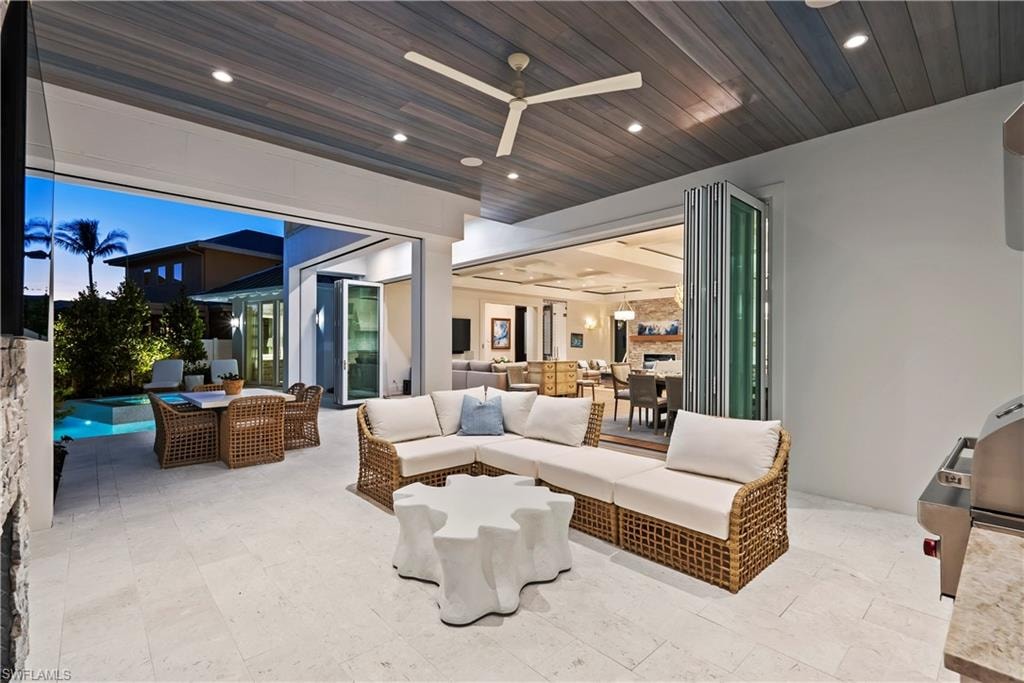 Patio terrace at dusk with exterior kitchen, an outdoor hangout area, and ceiling fan