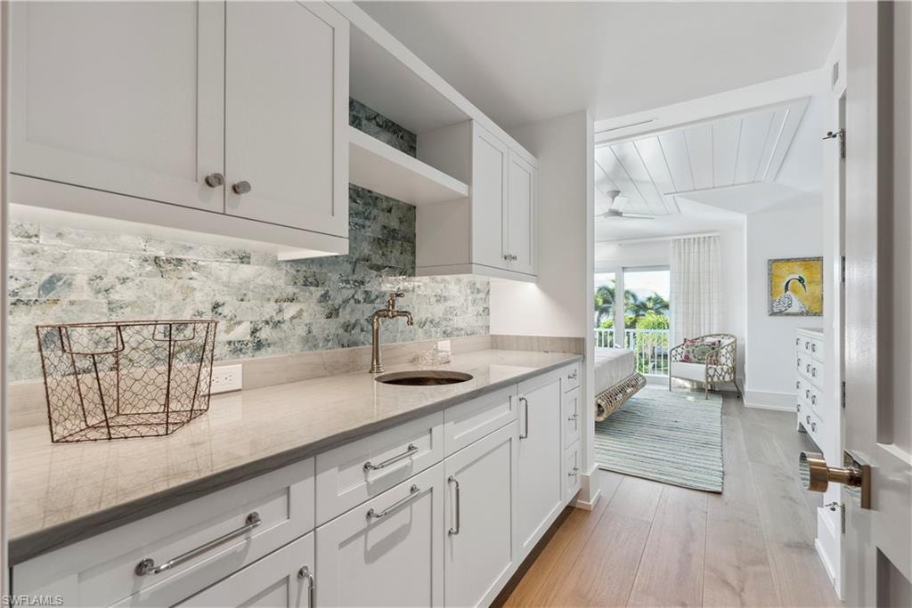 Kitchen with light stone countertops, sink, white cabinets, and light hardwood / wood-style floors