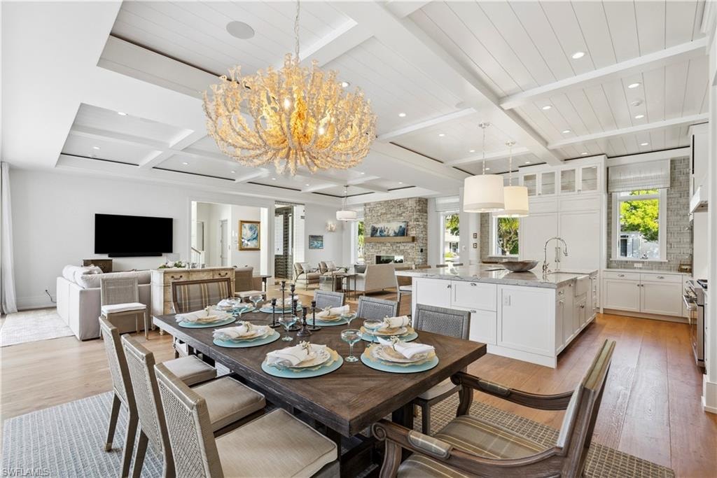 Dining area with beamed ceiling, a stone fireplace, sink, and light hardwood / wood-style flooring