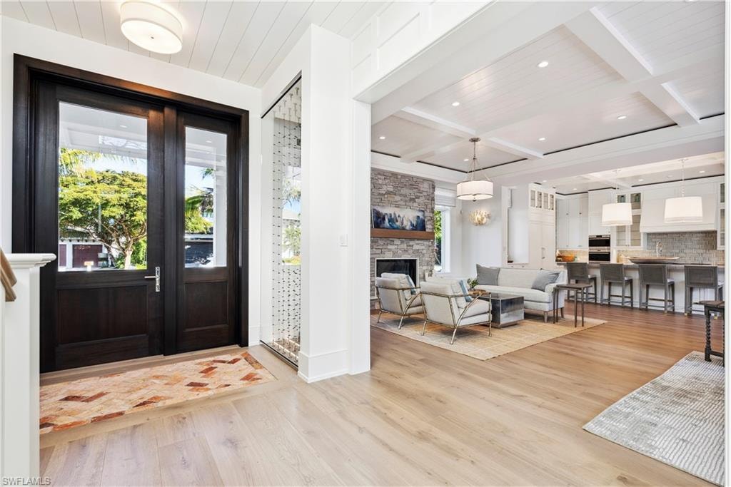Foyer with a stone fireplace, beamed ceiling, coffered ceiling, wooden ceiling, and light wood-type flooring