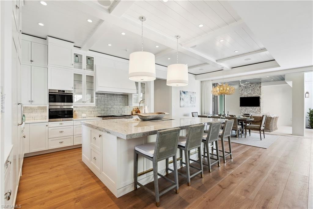 Kitchen with light stone countertops, decorative light fixtures, white cabinets, and a spacious island