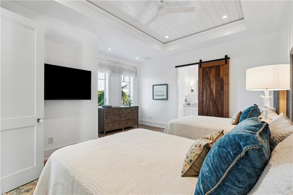 Bedroom featuring wood-type flooring, a barn door, connected bathroom, and a tray ceiling