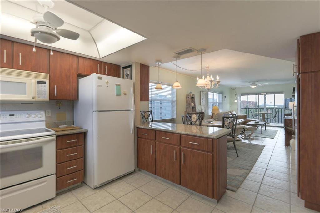 Kitchen with pendant lighting, white appliances, light tile floors, and ceiling fan with notable chandelier