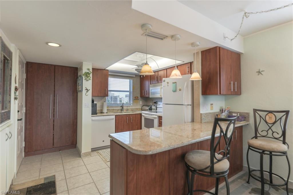Kitchen featuring hanging light fixtures, white appliances, kitchen peninsula, sink, and light tile flooring