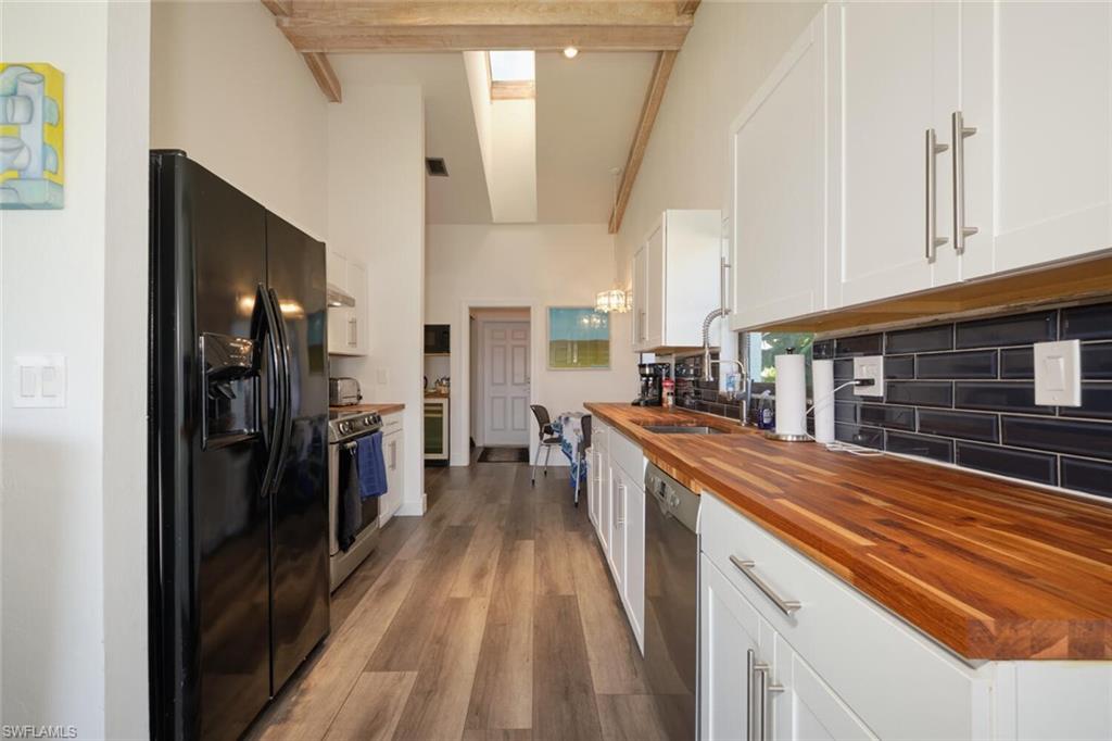 Kitchen featuring stainless steel appliances, tasteful backsplash, beam ceiling, light wood-type flooring, and wooden counters