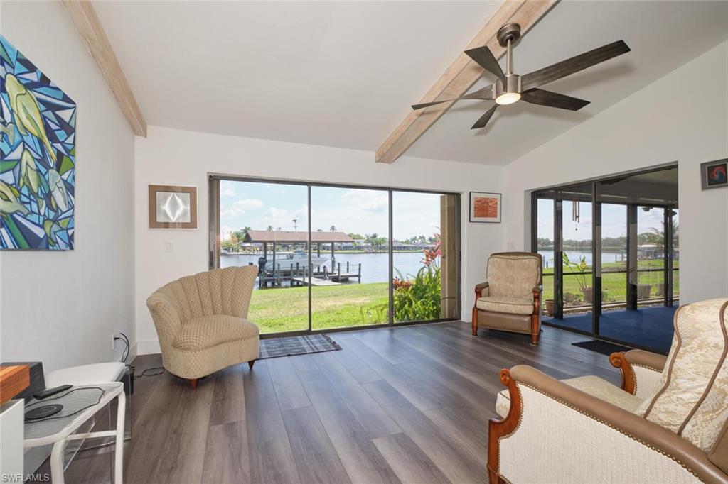 Living room featuring ceiling fan, vaulted ceiling with beams, a water view, and dark wood-type flooring