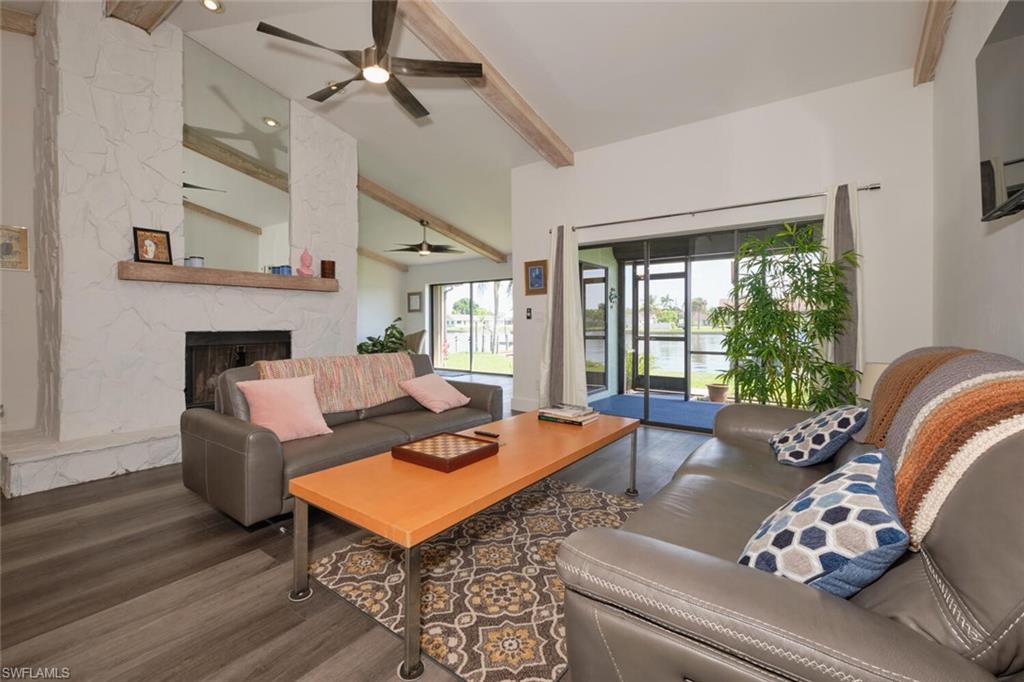Living room featuring a stone fireplace, lofted ceiling with beams, ceiling fan, and dark hardwood / wood-style floors