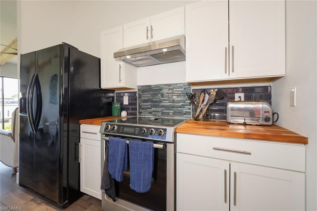 Kitchen featuring white cabinetry, electric range, dark hardwood / wood-style floors, black refrigerator with ice dispenser, and tasteful backsplash
