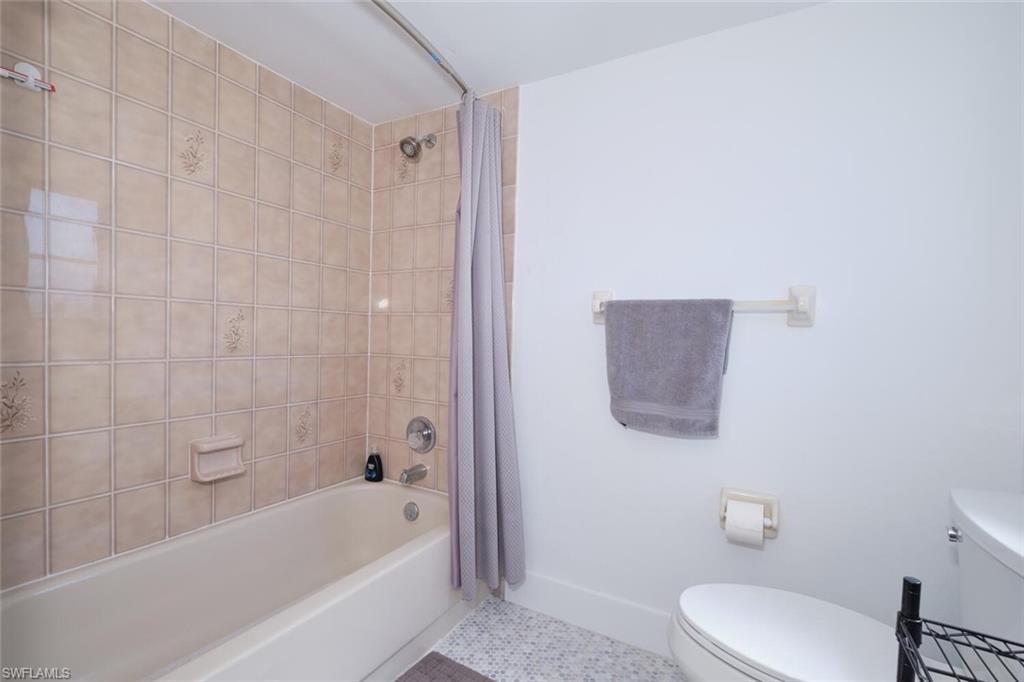 Bathroom featuring shower / bath combo with shower curtain, toilet, and tile floors