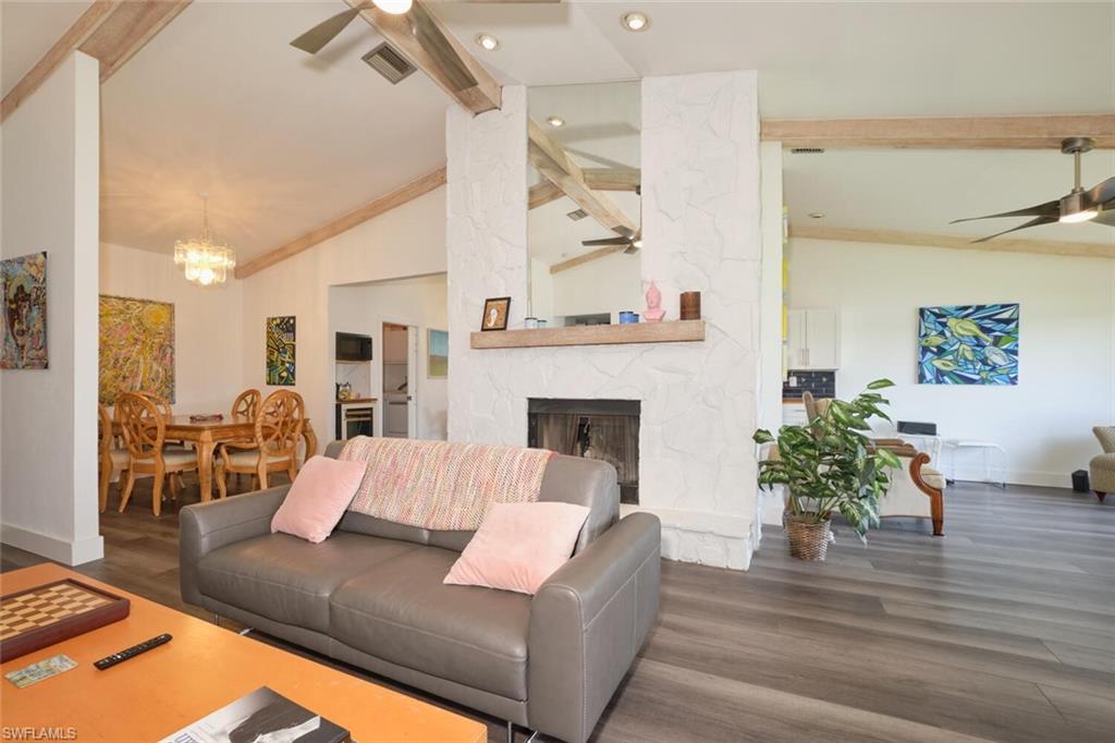 Living room featuring a fireplace, high vaulted ceiling, ceiling fan with notable chandelier, and dark hardwood / wood-style floors