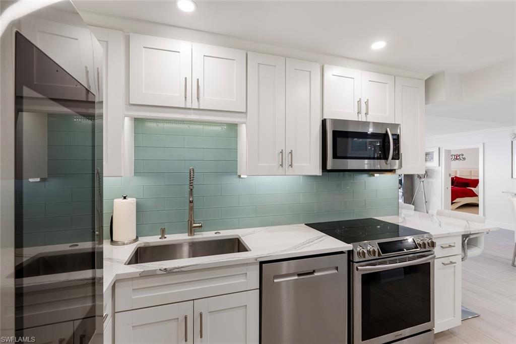 Kitchen featuring white cabinetry, stainless steel appliances, light stone counters, sink, and tasteful backsplash