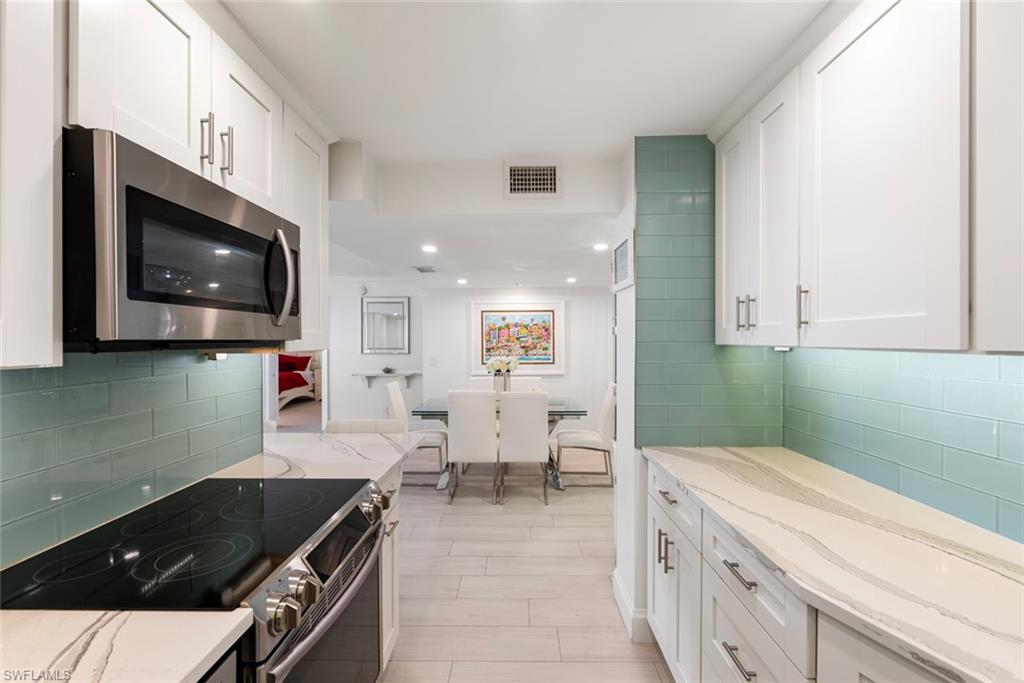Kitchen featuring stainless steel appliances, white cabinets, light stone countertops, and tasteful backsplash