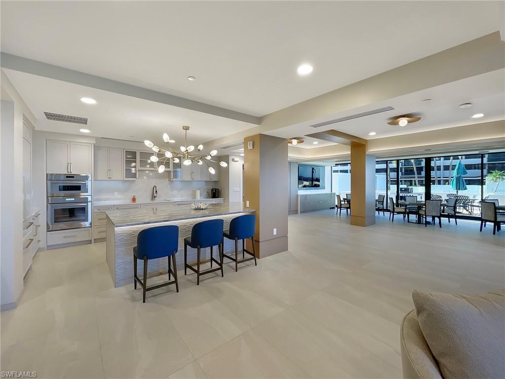 Community room kitchen with glass insert cabinets, open floor plan, a breakfast bar, white cabinets, and recessed lighting