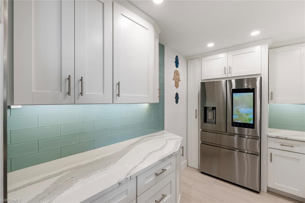 Kitchen featuring white cabinetry, stainless steel fridge with ice dispenser, tasteful backsplash, and light stone counters