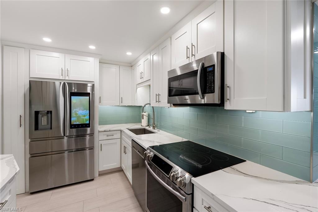 Kitchen featuring appliances with stainless steel finishes, white cabinetry, sink, and light stone countertops