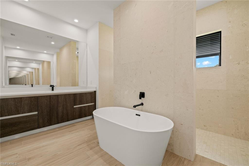 Full bath featuring tile walls, vanity, wood finished floors, walk in shower, and a freestanding bath