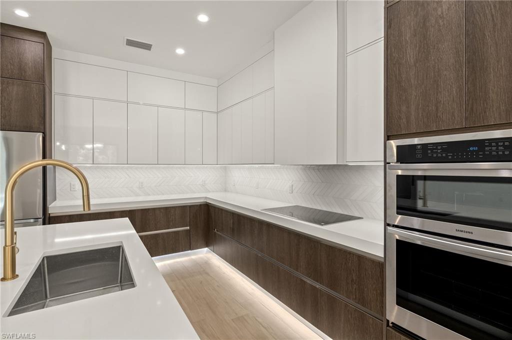 Kitchen featuring white cabinets, modern cabinets, a sink, dark brown cabinets, and double oven