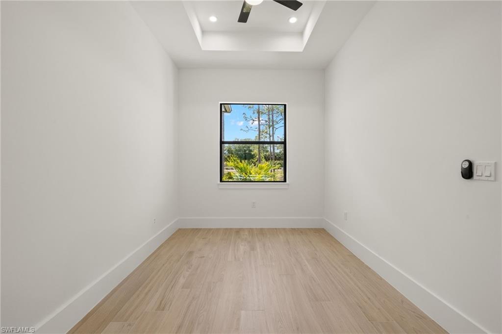 Empty room with light wood-style flooring, baseboards, a raised ceiling, and a ceiling fan