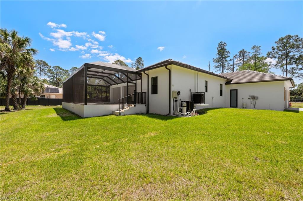 Back of property featuring a tiled roof, a yard, stucco siding, and glass enclosure