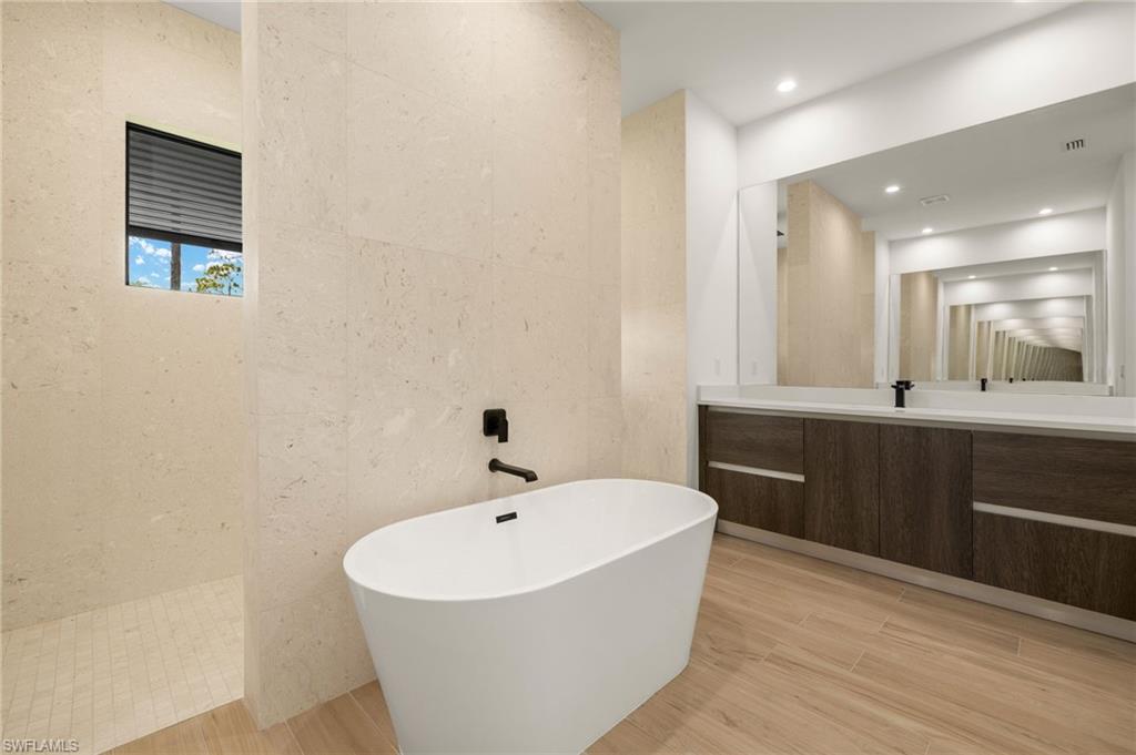 Full bath with vanity, a soaking tub, walk in shower, tile walls, and wood finished floors