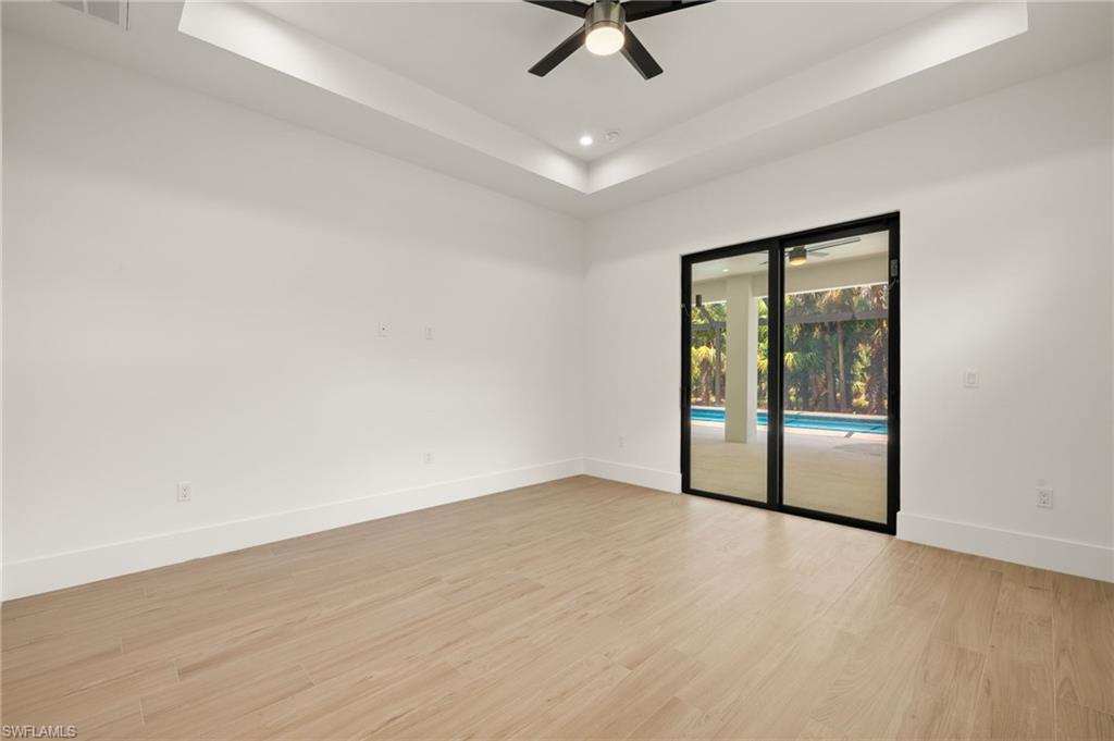 Spare room with a tray ceiling, baseboards, light wood-type flooring, and ceiling fan