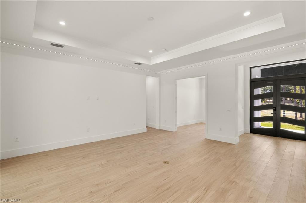 Empty room with light wood-style floors, recessed lighting, a raised ceiling, french doors, and baseboards