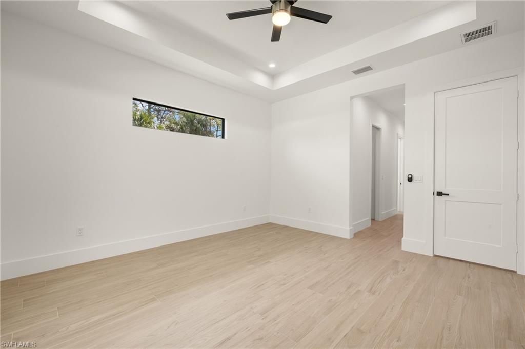Spare room with light wood-style floors, visible vents, a tray ceiling, and a ceiling fan
