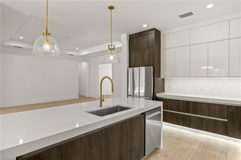 Kitchen with white cabinets, a sink, dark brown cabinetry, a tray ceiling, and stainless steel appliances