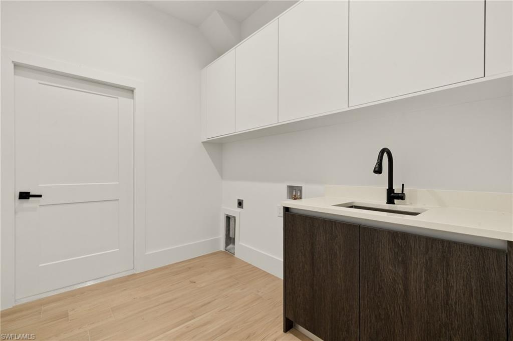 Laundry room with hookup for an electric dryer, hookup for a washing machine, cabinet space, light wood finished floors, and a sink