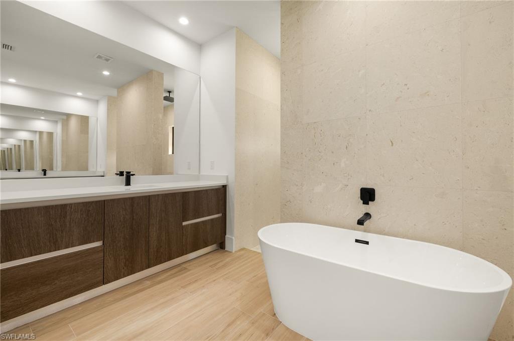 Full bath with a freestanding tub, vanity, visible vents, recessed lighting, and wood finished floors