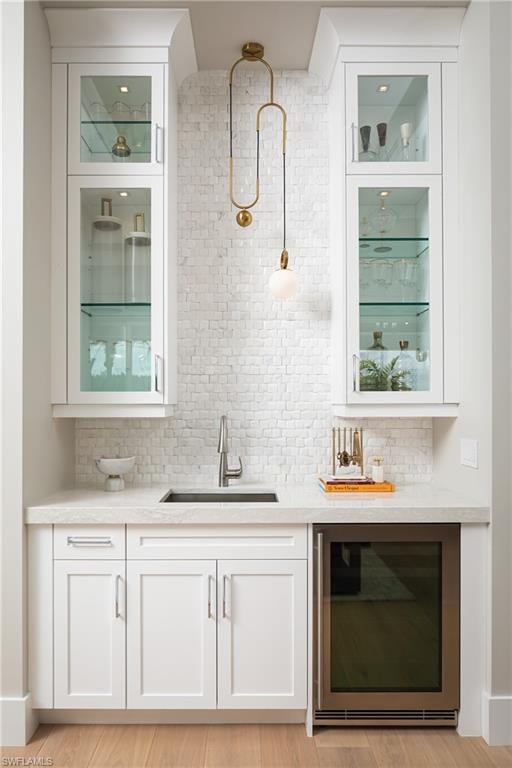 Bar featuring wine cooler, sink, tasteful backsplash, and light hardwood / wood-style flooring