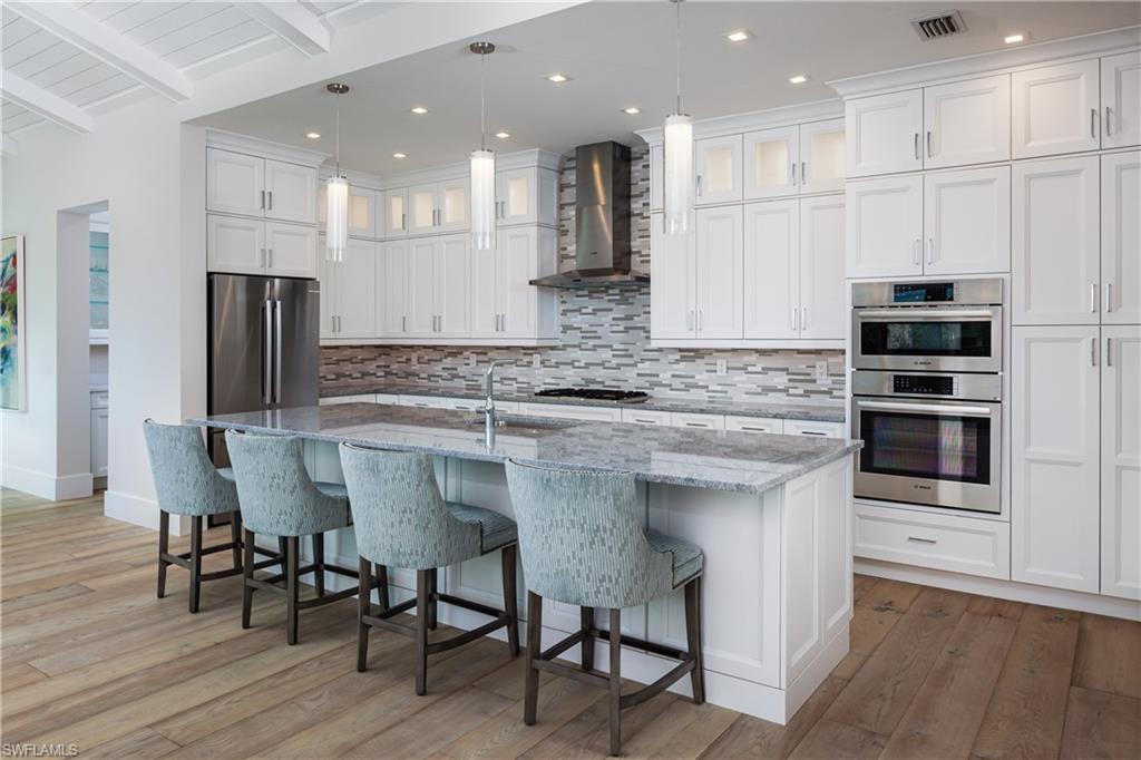 Kitchen with wall chimney exhaust hood, hardwood / wood-style flooring, pendant lighting, and appliances with stainless steel finishes