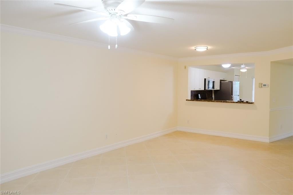 Tiled empty room with ceiling fan and ornamental molding