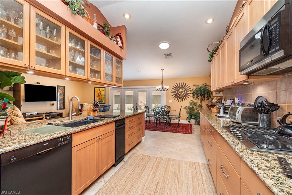 Kitchen featuring light stone countertops, stainless steel appliances, backsplash, light tile floors, and hanging light fixtures