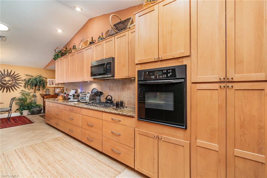 Kitchen with black appliances, backsplash, light tile flooring, vaulted ceiling, and light brown cabinets