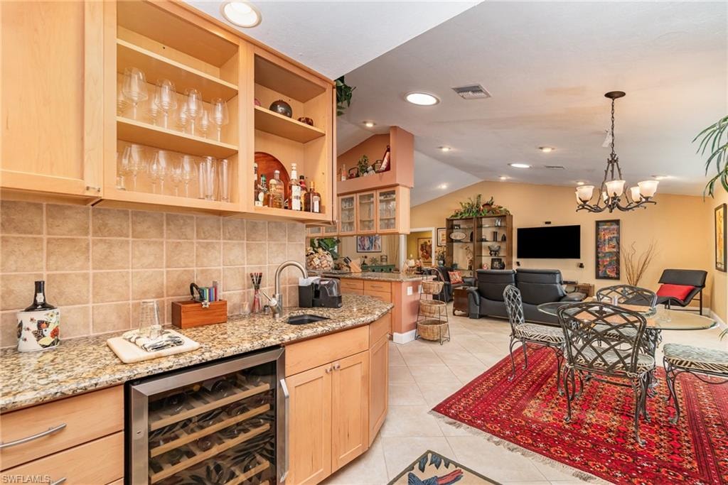 Kitchen with light stone countertops, beverage cooler, backsplash, sink, and light tile flooring