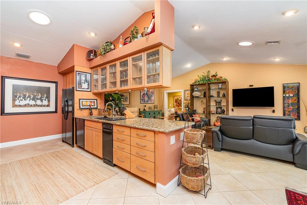 Kitchen featuring light stone countertops, lofted ceiling, black appliances, kitchen peninsula, and light tile floors