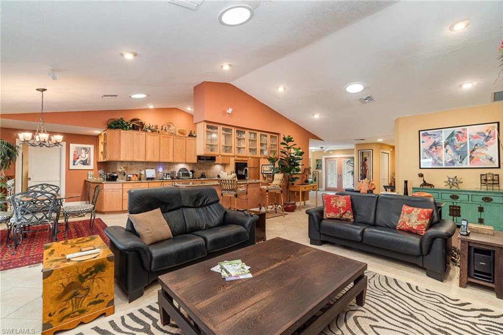 Living room featuring vaulted ceiling, a chandelier, and light tile flooring