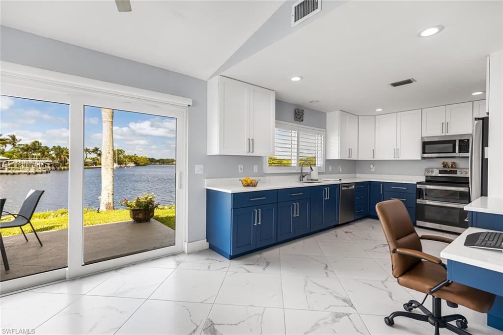 Kitchen with a river view, blue cabinetry, white cabinetry, quartz counter tops, stainless steel appliances, porcelain tile floors.  Built in desk on right side of photo.