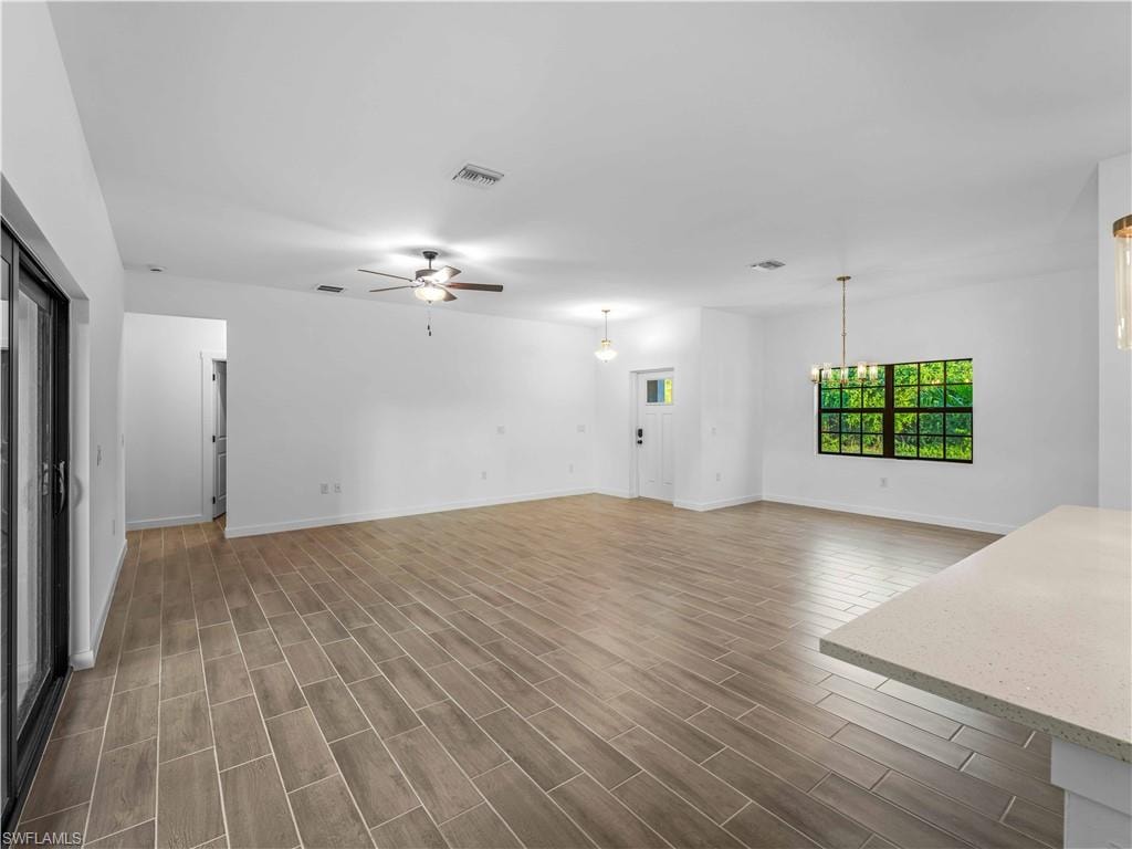 Unfurnished living room featuring a ceiling fan, dark wood-style flooring, baseboards, and a chandelier