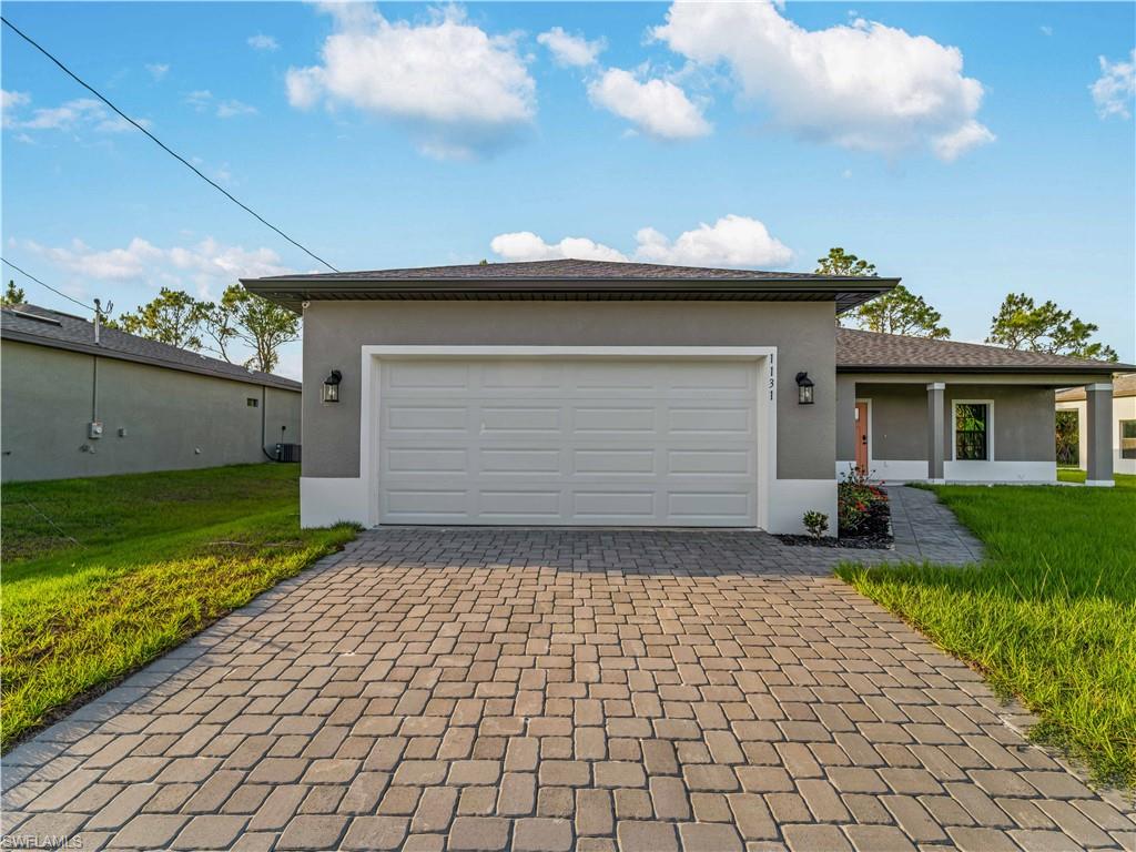 Single story home featuring stucco siding, decorative driveway, a front lawn, and an attached garage