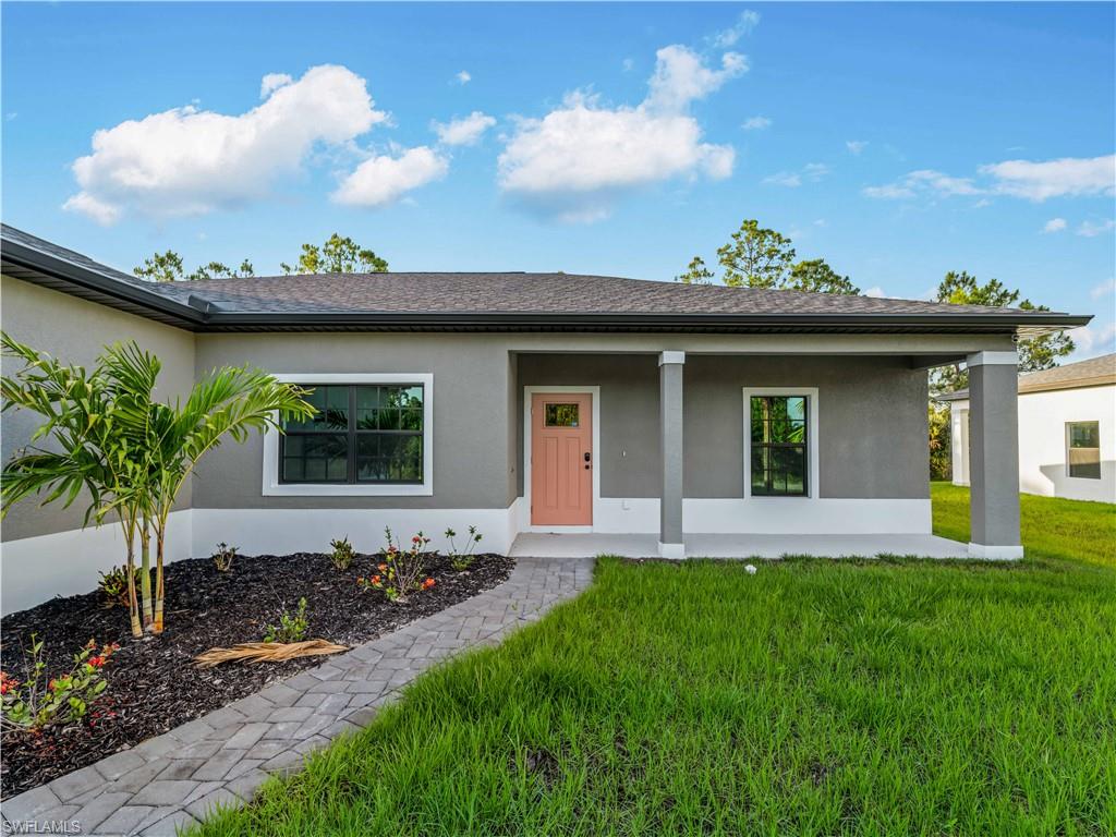 Ranch-style house featuring stucco siding, a front yard, covered porch, and roof with shingles