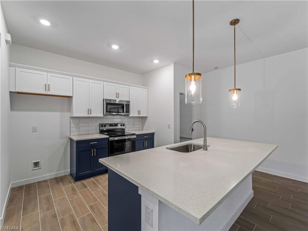 Kitchen with stainless steel appliances, a sink, blue cabinets, wood tiled floors, and baseboards
