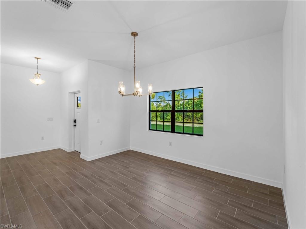 Spare room with a chandelier, baseboards, and dark wood-type flooring
