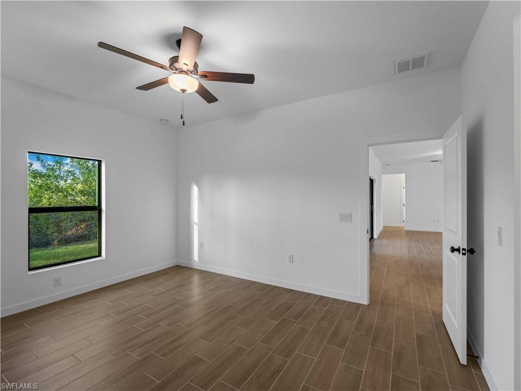 Empty room featuring dark wood-style flooring, a ceiling fan, and baseboards