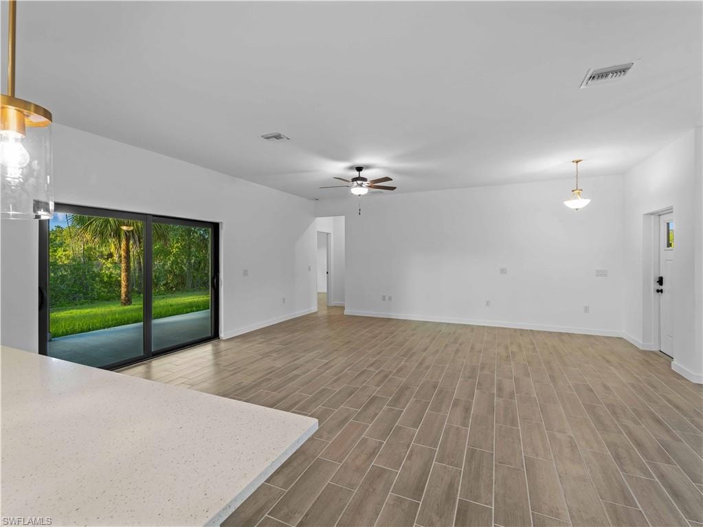 Unfurnished living room featuring a ceiling fan, wood finished floors, and baseboards