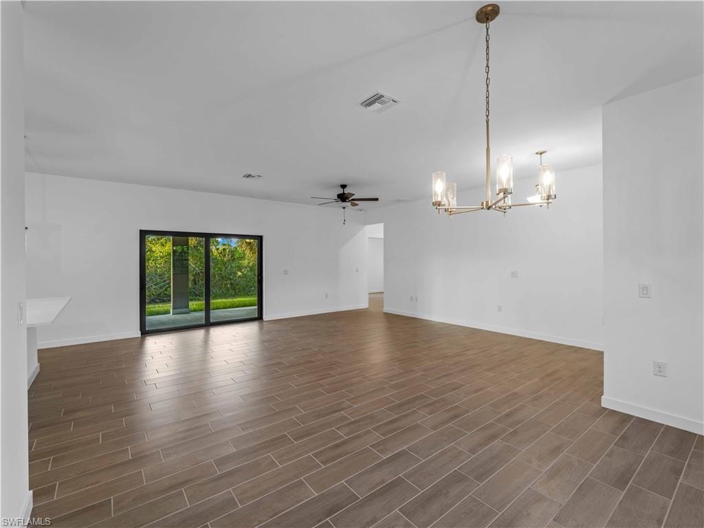 Empty room featuring a chandelier, dark wood finished floors, and baseboards