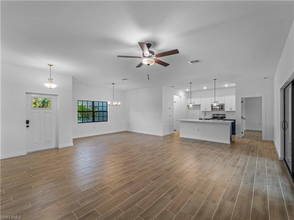 Unfurnished living room featuring ceiling fan, baseboards, recessed lighting, wood finished floors, and a chandelier