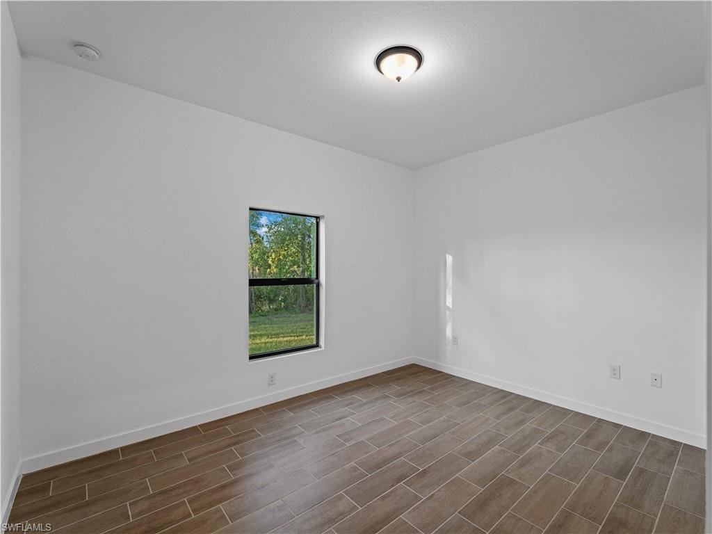 Empty room with dark wood-style floors, a smoke detector, and baseboards