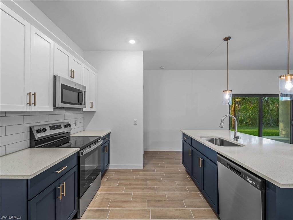 Kitchen with appliances with stainless steel finishes, a sink, baseboards, backsplash, and wood finish floors
